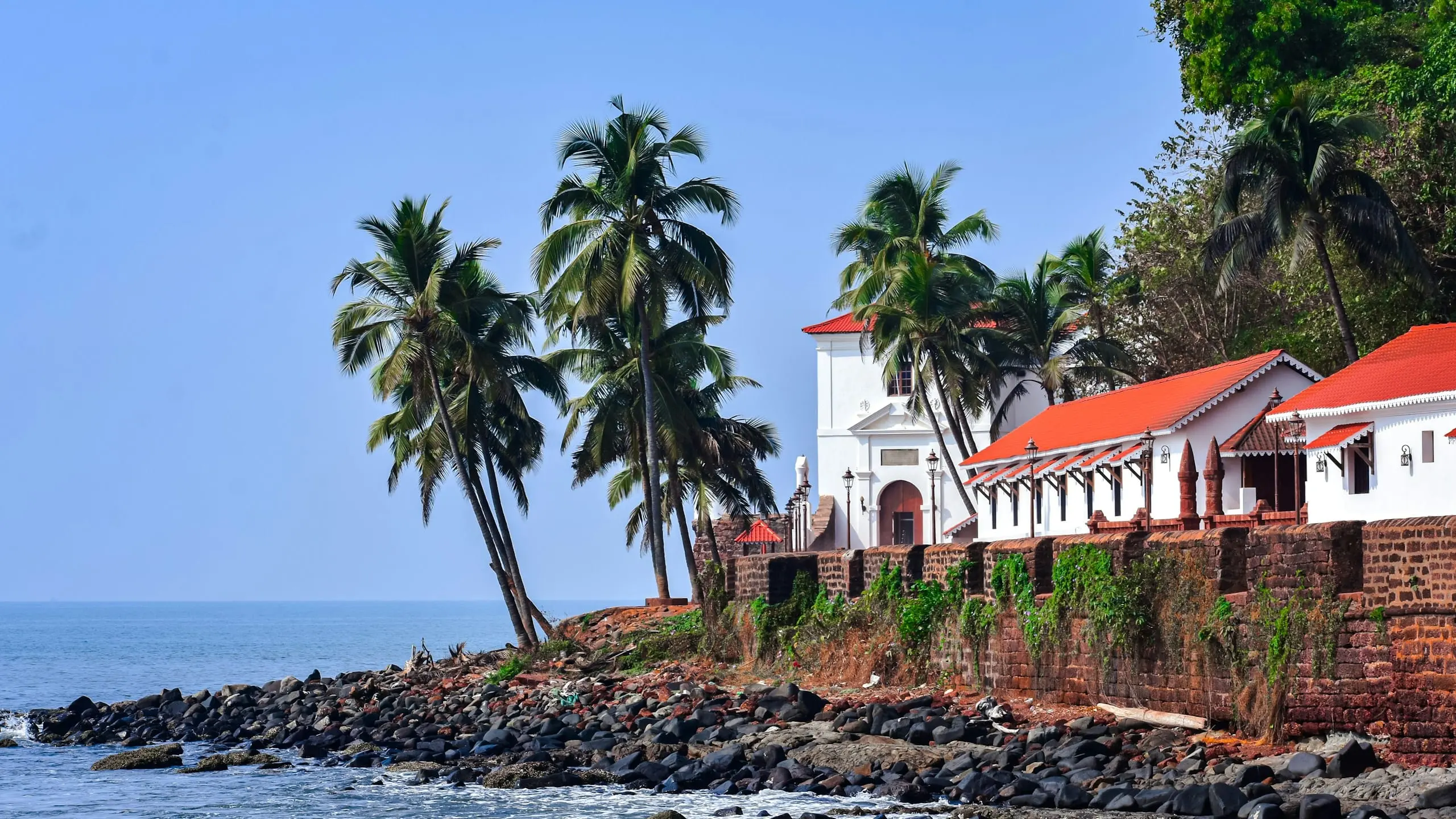 A red-roofed chapel beside the sea framed by palm trees