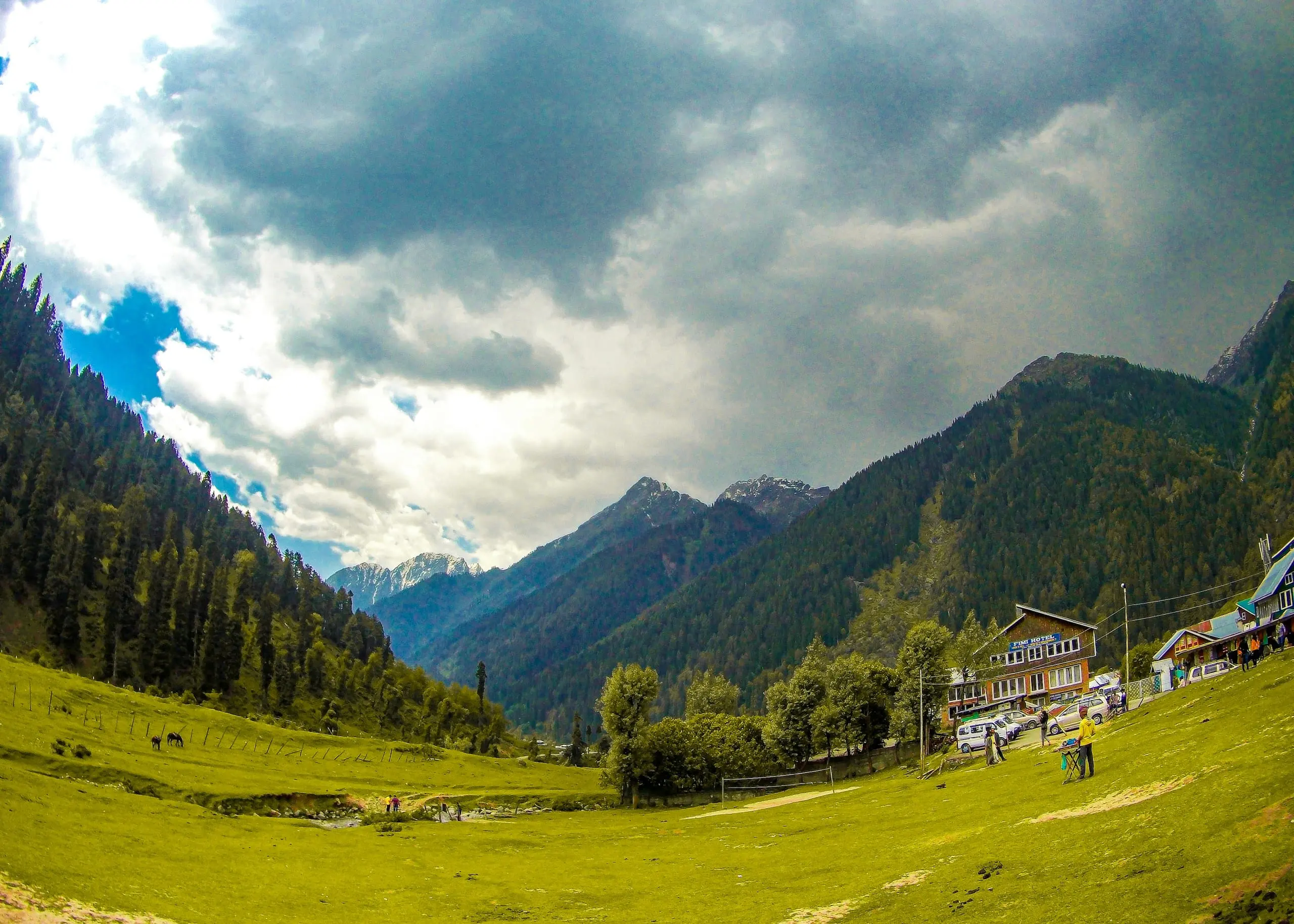 A green valley and river in Pahalgam under dramatic clouds