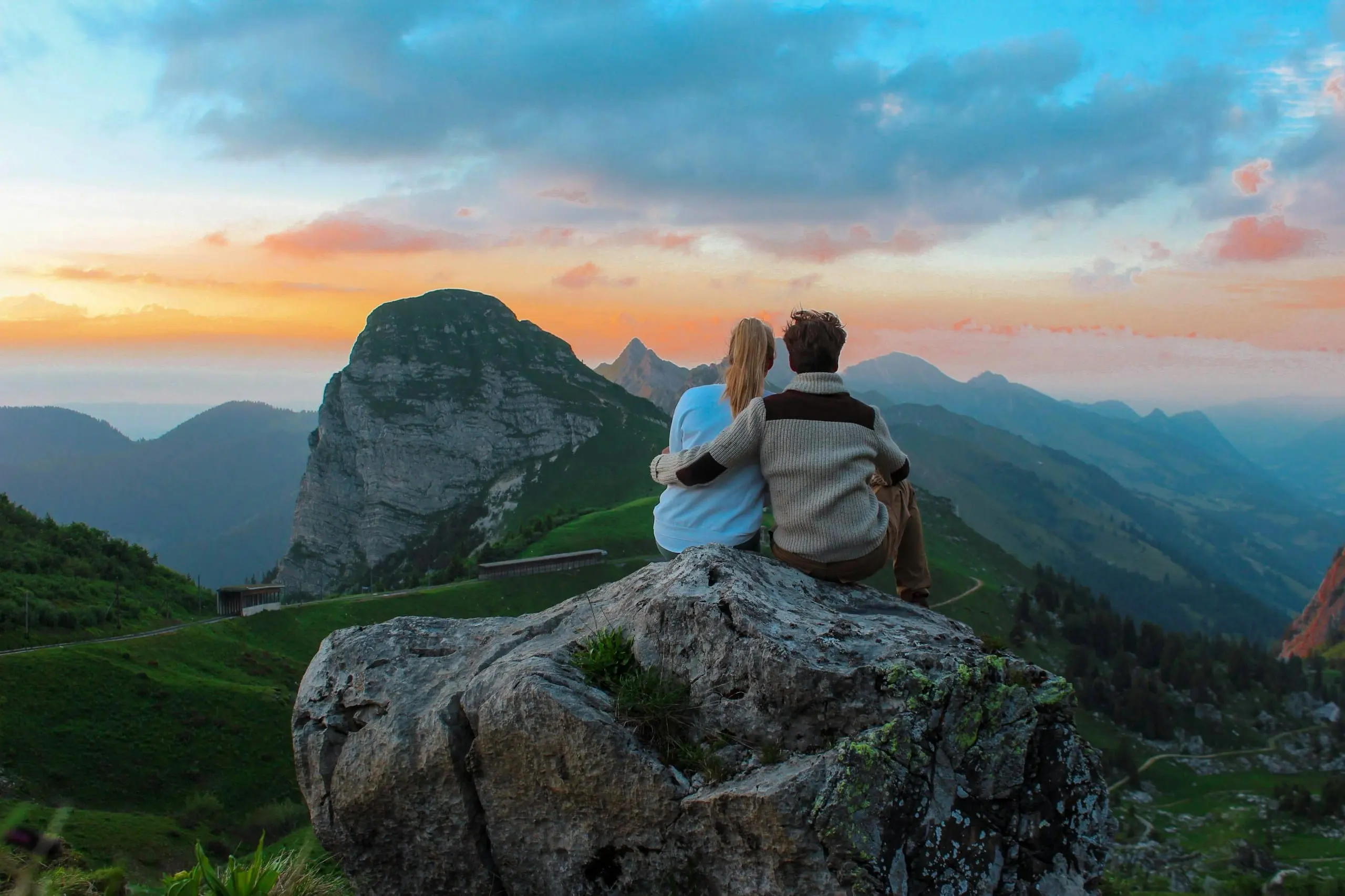 A couple sitting together on a rock watching the sunset over mountains